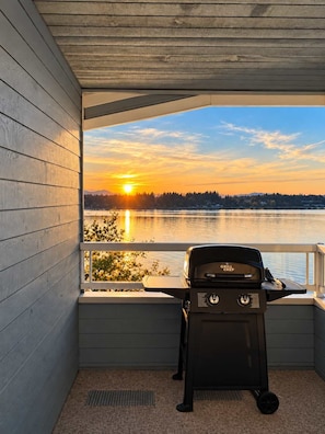 A grill on a balcony overlooking a body of water with a sunset. - Seaside Cedar Escape (Nanoose Bay)
