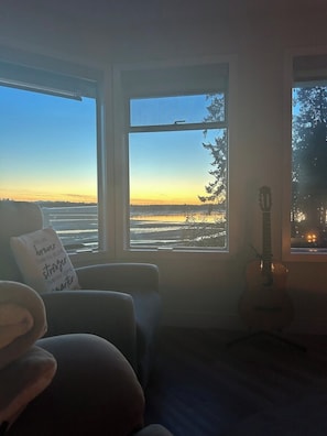 Ein Zimmer mit Blick auf einen Sonnenuntergang über dem Wasser, einer Gitarre und einem Sessel mit Kissen.