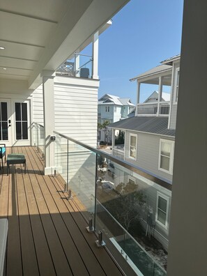 Eine Holzterrasse mit Glasgeländer, die auf einen Wohnbereich blickt.