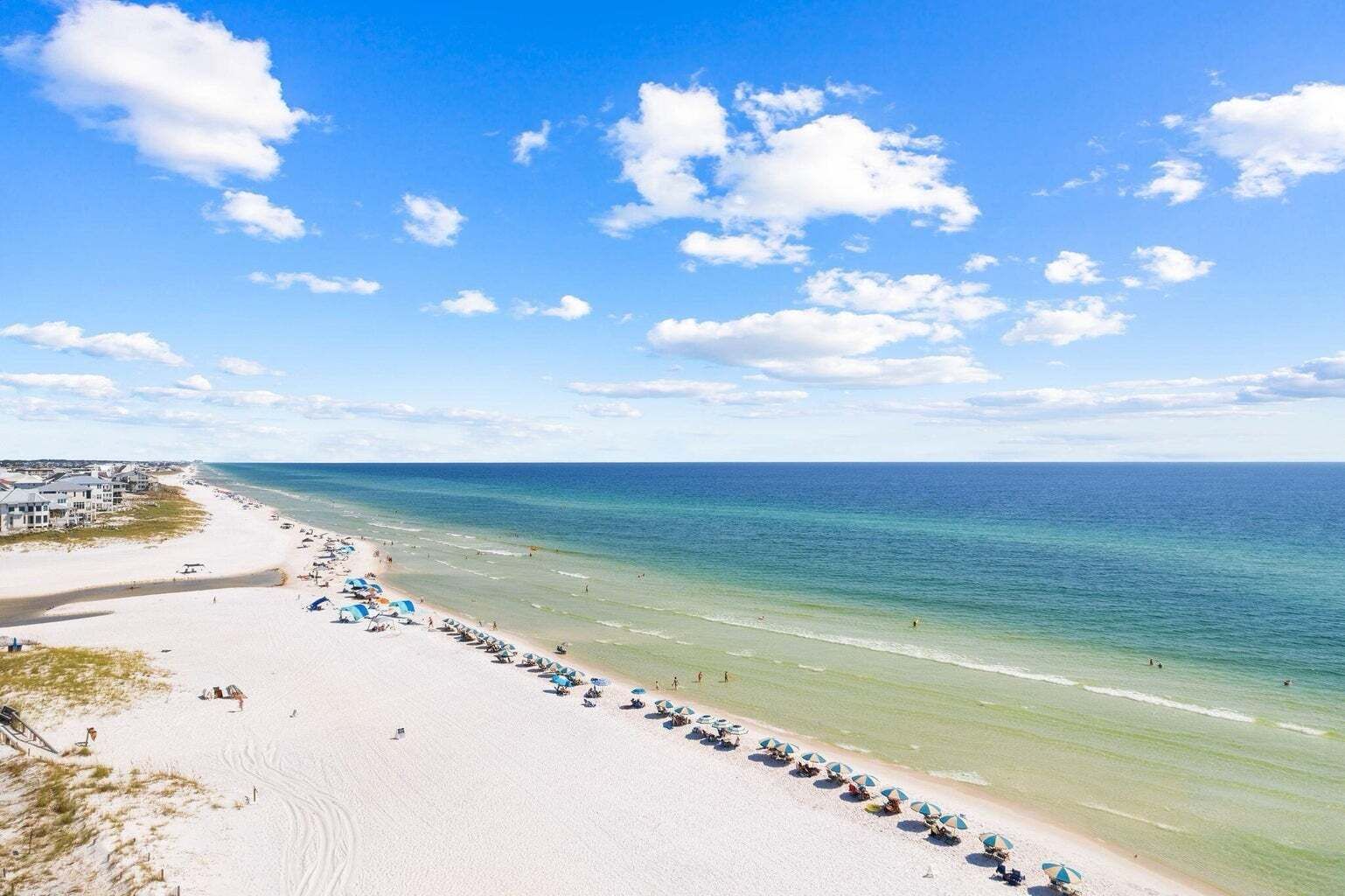 Ein Strand mit einer Reihe von Sonnenschirmen und Liegestühlen, wolkenlosem Himmel und dem Meer.