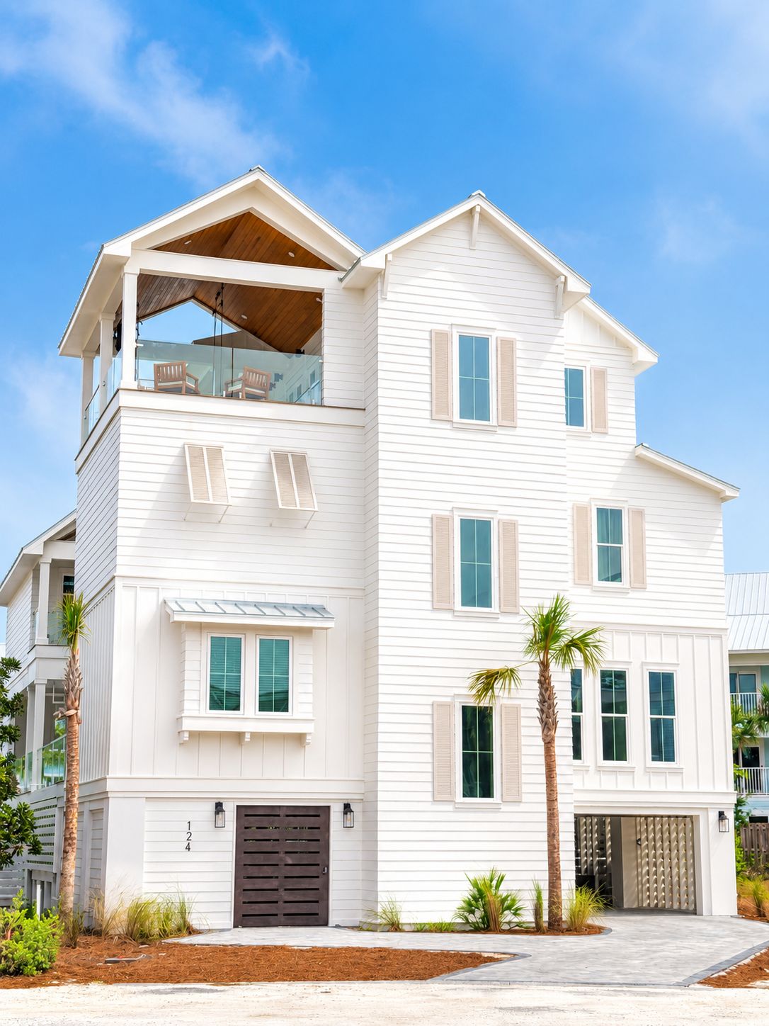 Une maison à deux étages avec un balcon, un garage et un jardin devant, agrémenté de palmiers.