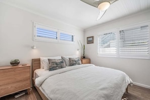 A bedroom with a large bed, two bedside tables, a nightstand, and two windows with blinds. - Absolute Beachfront Apartment 11B (Lennox Head)