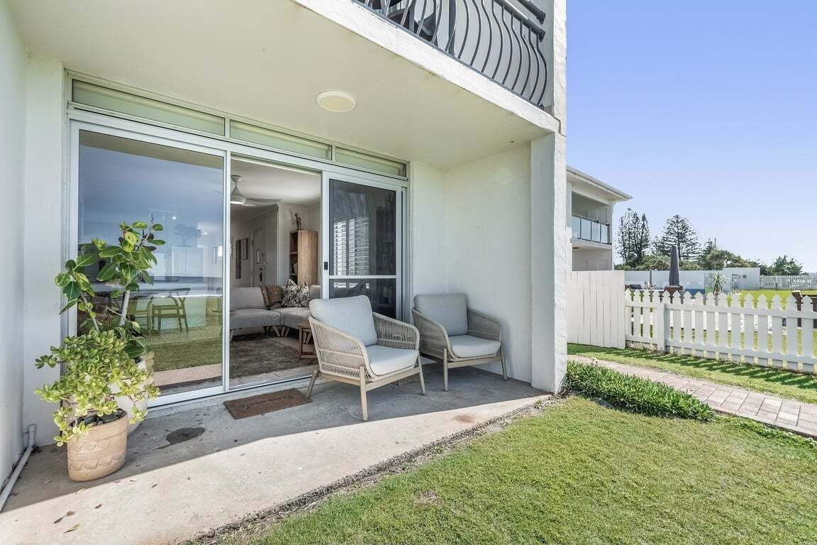 Een modern gebouw met balkon, schuiframen en terrasmeubels.