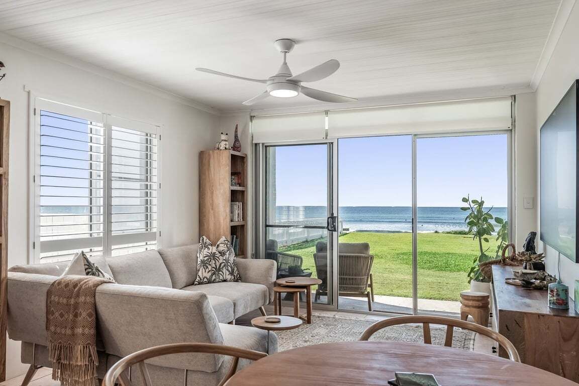 A living room with a large sliding glass door leading to a balcony with a view of the ocean.