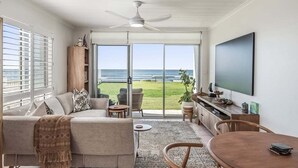 Ein modernes Wohnzimmer mit Sofa, Couchtisch und Fernseher, mit Balkon und Blick aufs Meer.