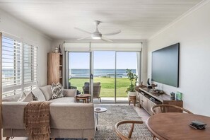 Ein modernes Wohnzimmer mit Sofa, Couchtisch und Fernseher, mit Balkon und Blick aufs Meer.