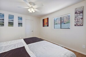 Ein Schlafzimmer mit einem Bett, einem Deckenventilator und Kunstwerken an den Wänden.