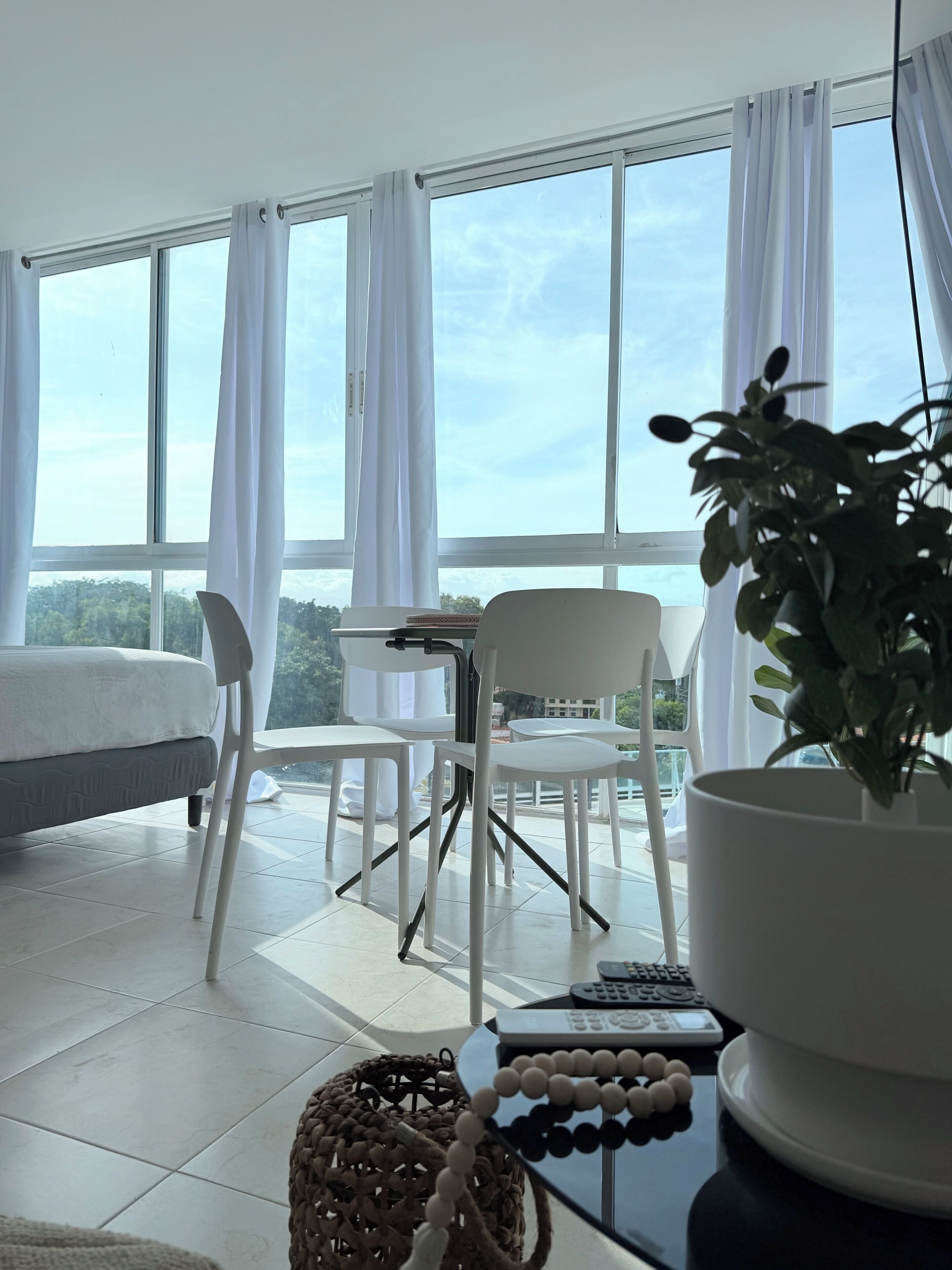Une chambre avec un lit, une table ornée d’une plante et une vue sur l’extérieur grâce à de grandes fenêtres.