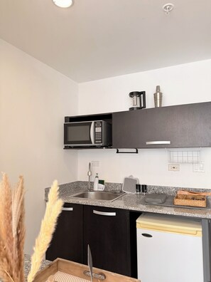 Una cocina compacta con microondas, lavamanos y un refrigerador pequeño.