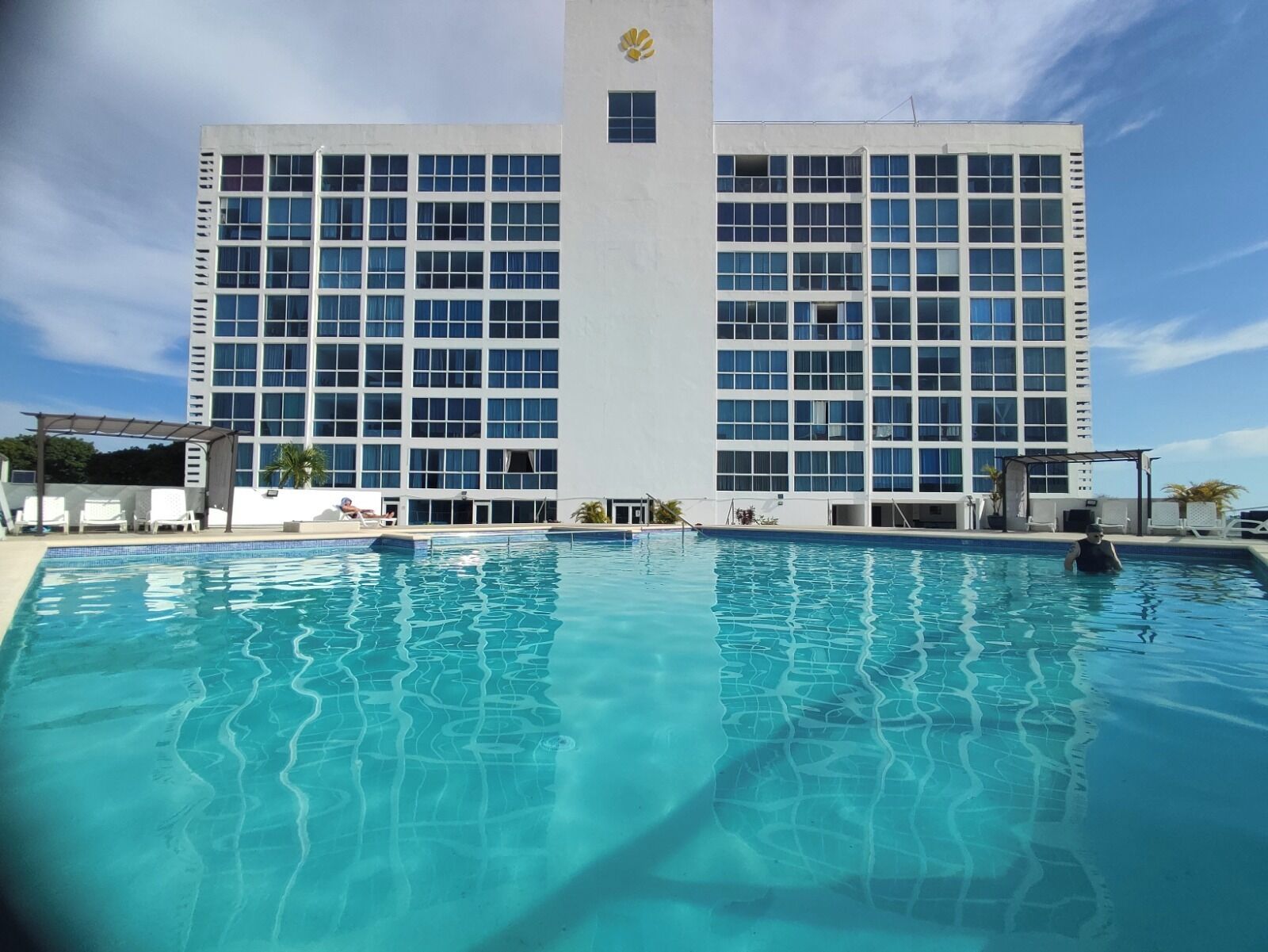 Un hotel con una piscina grande, fachada de edificio moderna y cielo despejado.