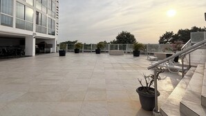 A rooftop terrace with a modern building, potted plants, and outdoor seating.