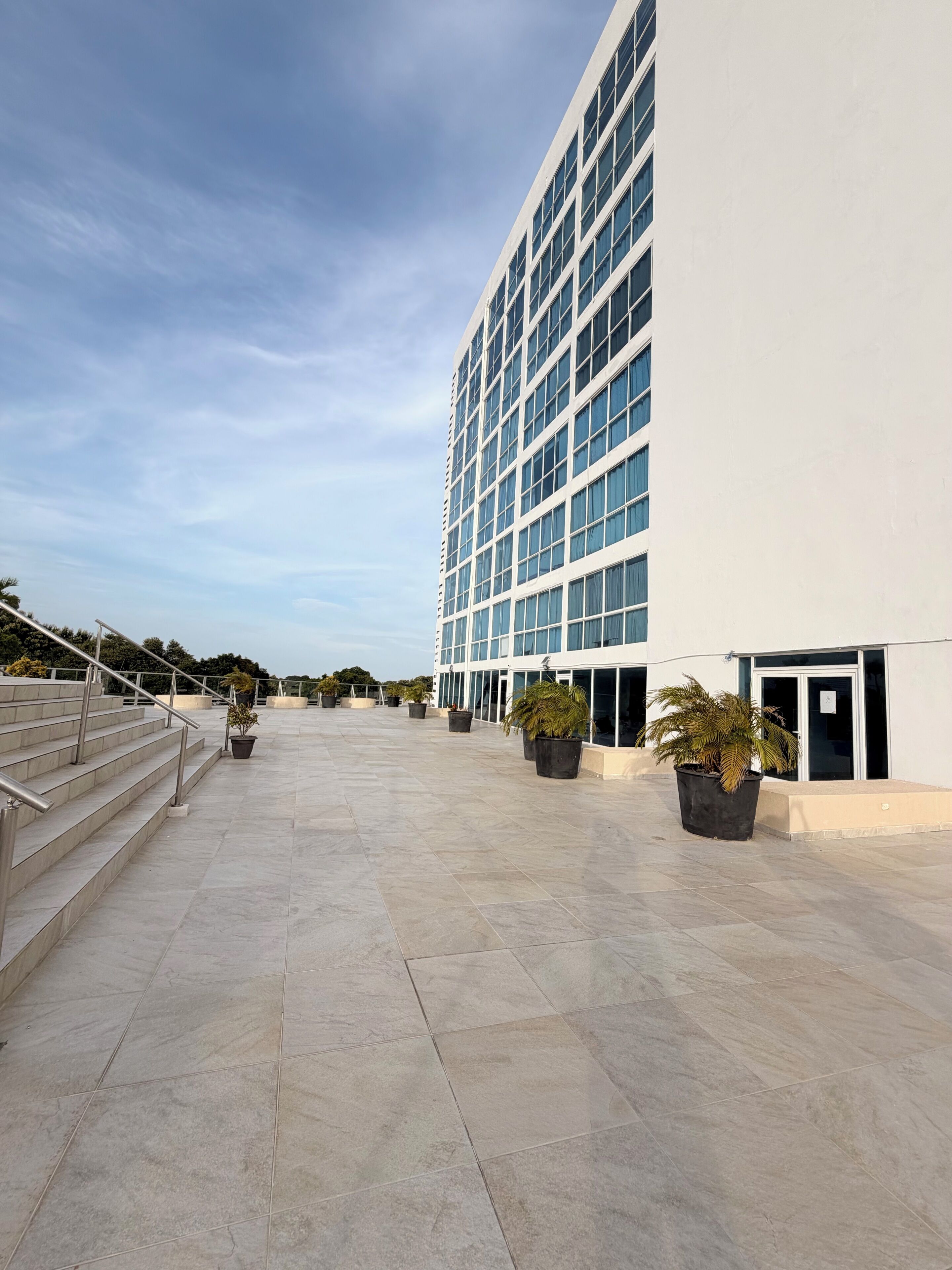 Un edificio moderno con terraza plana, plantas en macetas y una escalera.