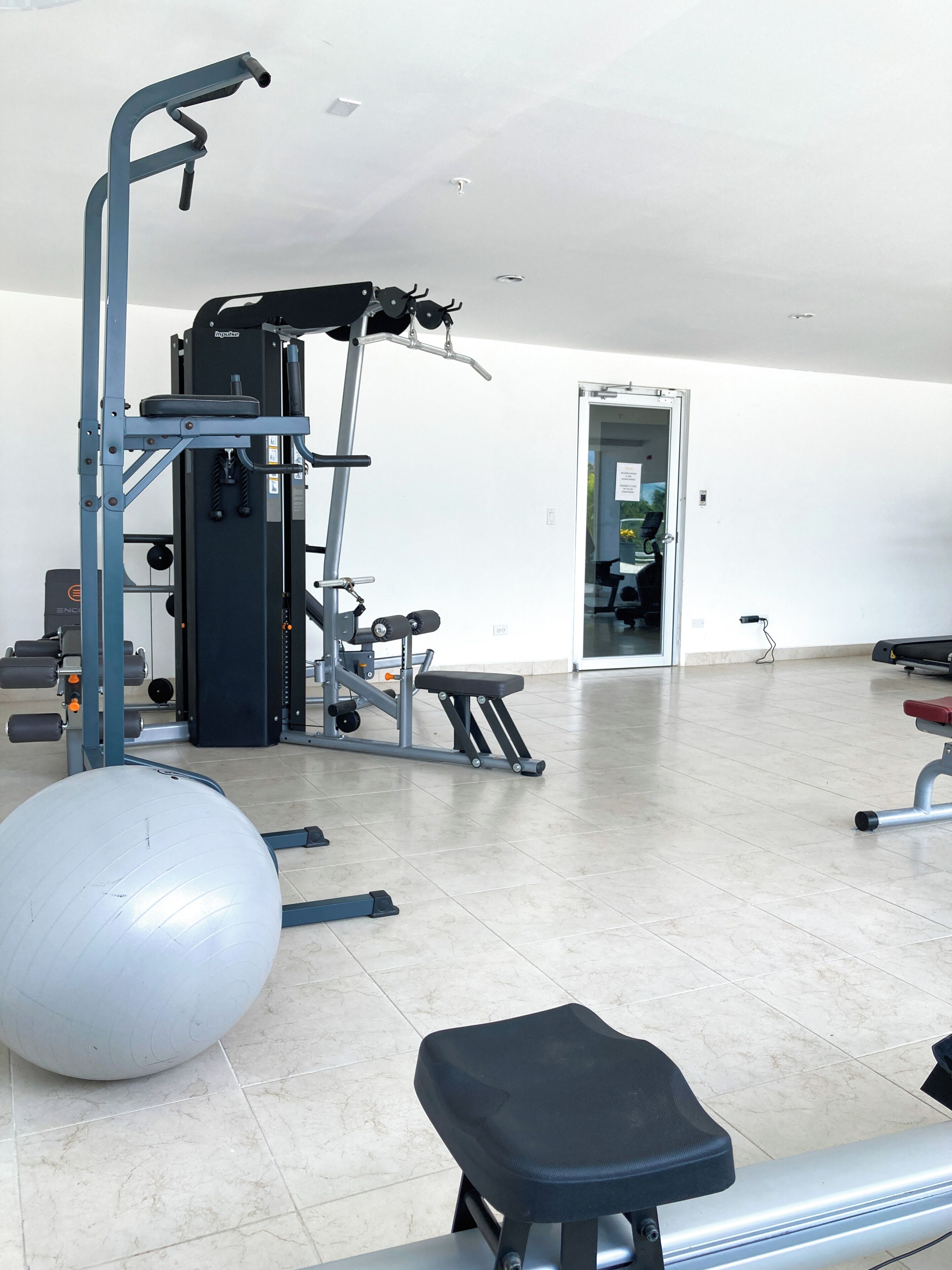 Un gimnasio con equipo de ejercicio, una pelota grande para hacer ejercicio y una banca.