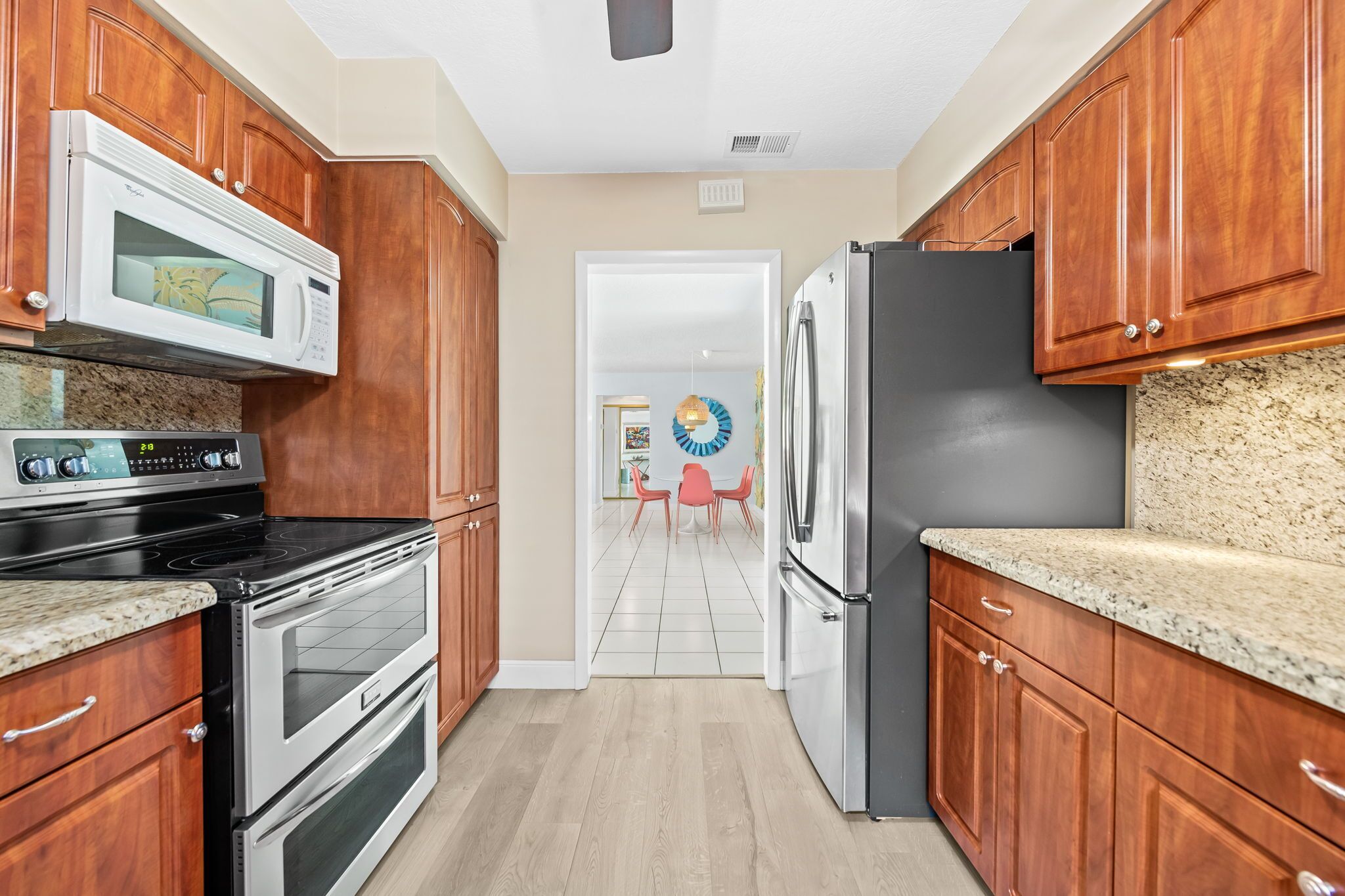 A kitchen with wooden cabinets, a microwave, stove, refrigerator, and a dining area with a table and chairs.