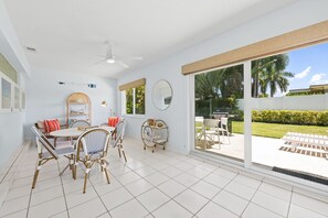 A spacious room with a dining area, a ceiling fan, and a view of a backyard with a grill. - 1980s Retro Home ~ 12 Minute Walk to Beach: 2BR/2BA with kitchen, WiFi, parking, and patio. (Pompano Beach)