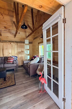 Ein Holzinterieur mit einer Couch, Sesseln, einem roten Flamingo und einer Schiebetür aus Glas.