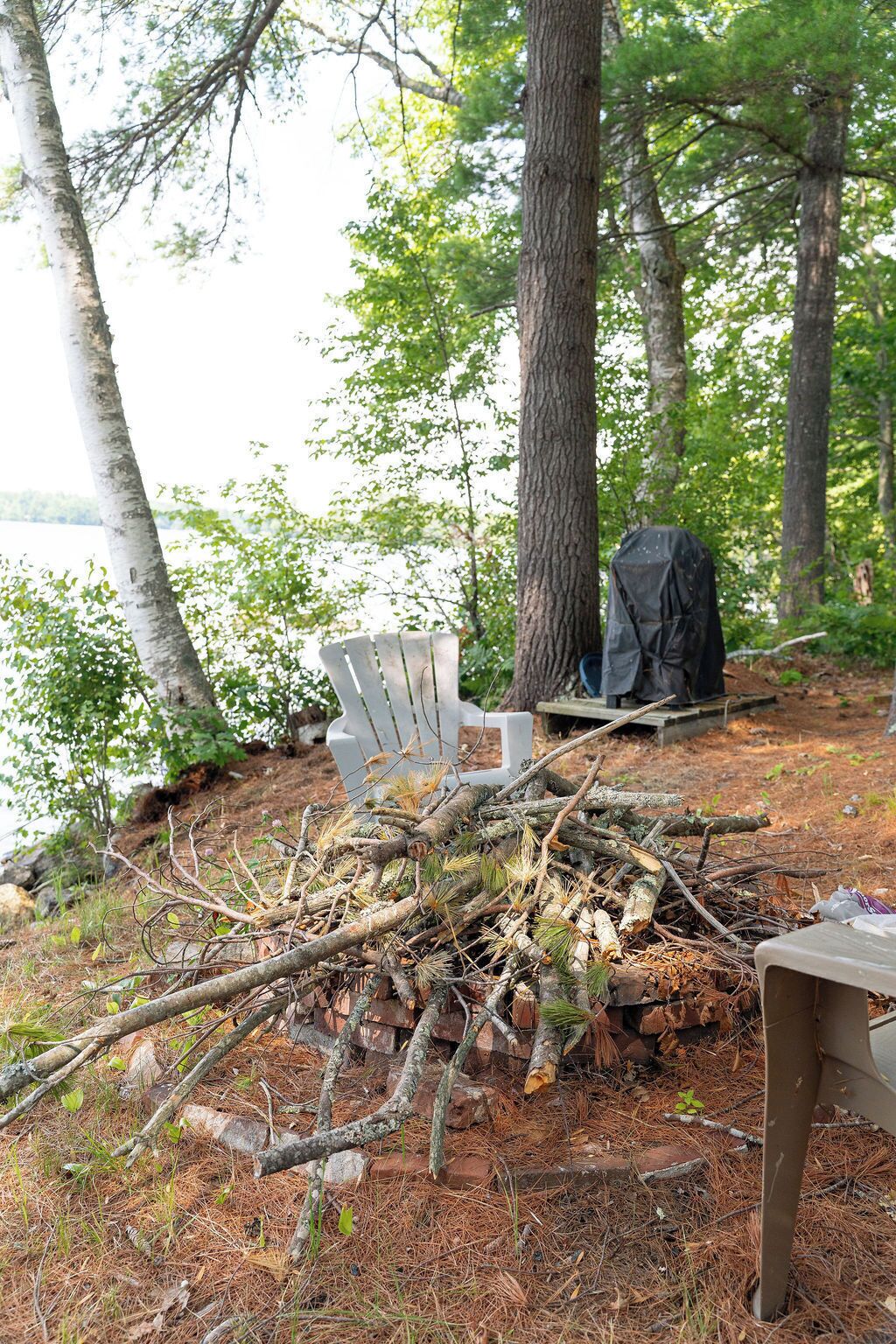 A campsite with a white chair, a black tarp, and a pile of branches.