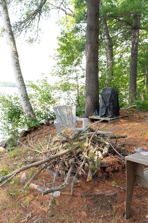 A campsite with a white chair, a black tarp, and a pile of branches.