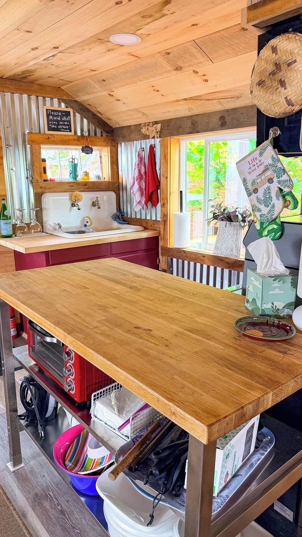 A rustic kitchen with a wooden table, a red oven, and a window with a view of greenery.