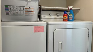 A laundry area with a washing machine and dryer, a notice about usage restrictions, and cleaning products on the dryer. - Cozy Inner Richmond Apartment, Steps to Golden Gate Park (San Francisco)