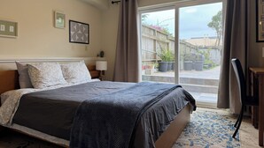 A bedroom with a large bed, a nightstand, a lamp, a chair, and a view of the outside. - Cozy Inner Richmond Apartment, Steps to Golden Gate Park (San Francisco)