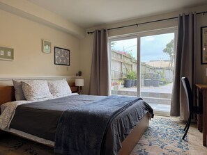 Ein Schlafzimmer mit einem großen Bett, einem Nachttisch, einer Lampe, einem Sessel und Blick ins Freie.