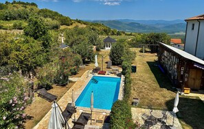 A swimming pool with lounge chairs and umbrellas, surrounded by greenery and a view of hills. - Awesome home in Vizinada with private swimming pool, can be inside or outside (Vizinada)