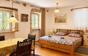 Une chambre à coucher avec un lit en bois, une table, une chaise et une fenêtre avec des rideaux.