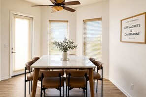 Une salle à manger avec une table en marbre, six chaises, un ventilateur de plafond et une plante en pot.