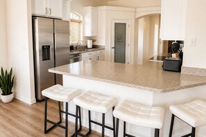Una cocina moderna con refrigerador de acero inoxidable, encimera de granito y taburetes de bar blancos.