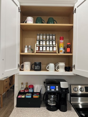 Une cuisine équipée d’une machine à café, d’une cuisinière et d’un placard contenant des épices et des condiments.