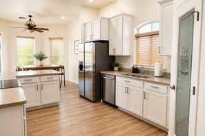 Una cocina moderna con armarios blancos, un refrigerador de acero inoxidable y una zona de comedor con una mesa y sillas.