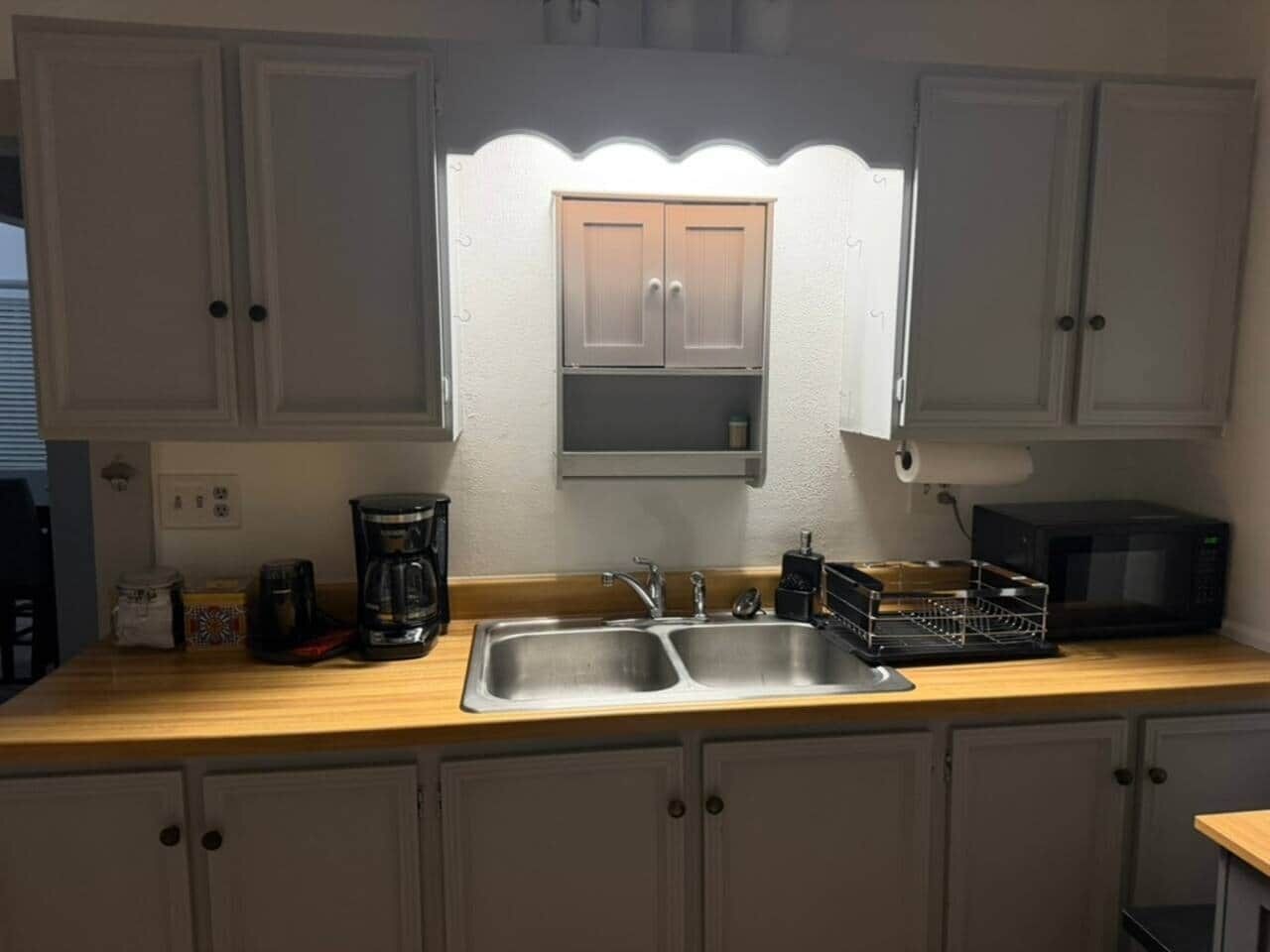 A kitchen with a double sink, a coffee maker, a microwave, and cabinets.