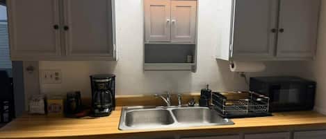 A kitchen with a double sink, a coffee maker, a microwave, and cabinets.