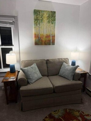 Sala de estar com sofá, duas luminárias, um quadro e uma janela.