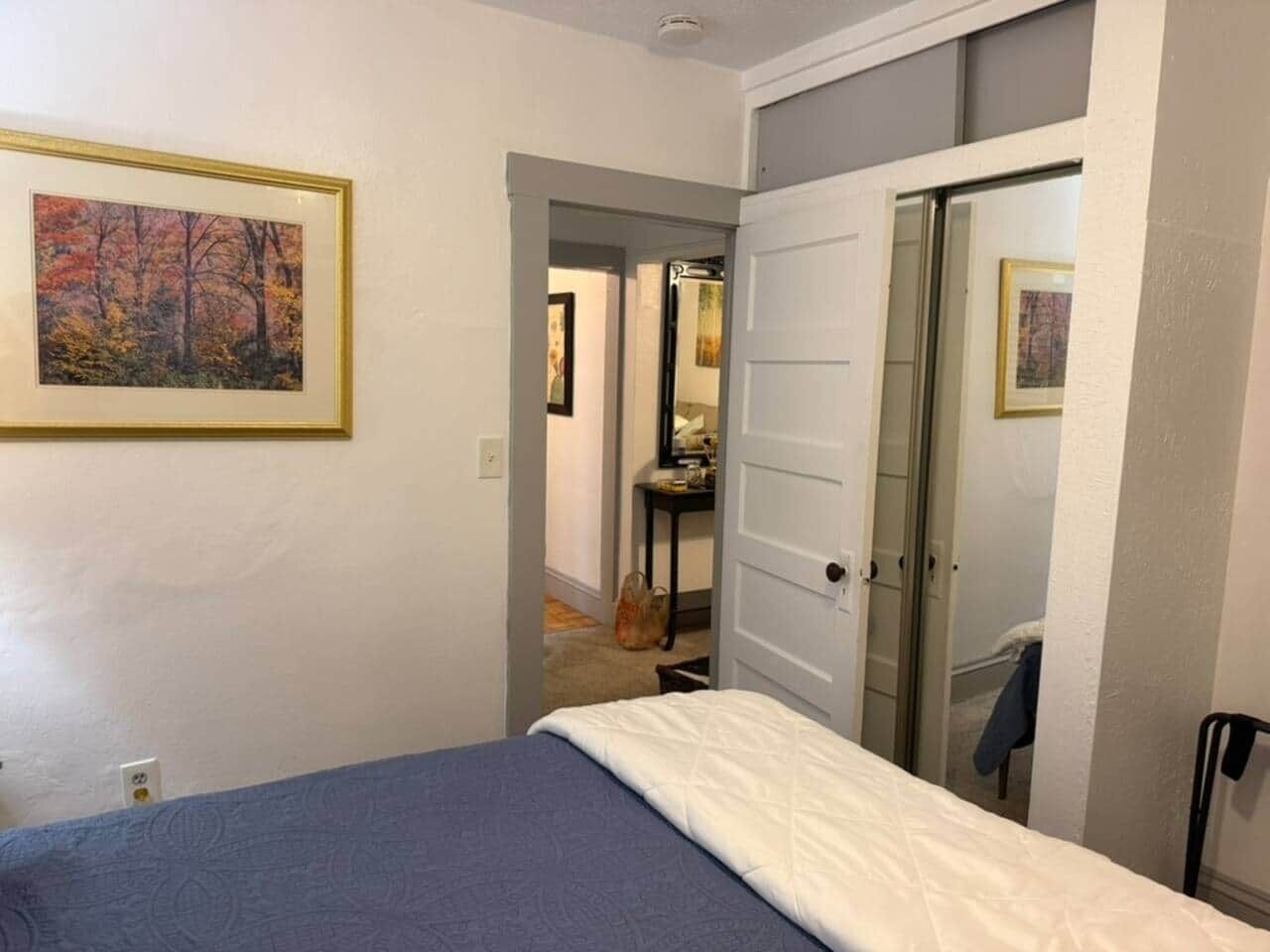 A bedroom with a bed, a door leading to a bathroom, and a framed picture on the wall.