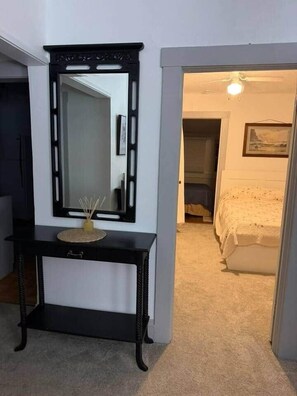 A hallway with a black console table, a mirror, and a bed in the adjacent room. - NEW Listing Half Block to Downtown Treetop Apt 3bd (Black Mountain)