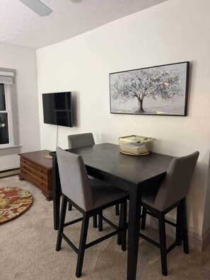 Uma área de jantar com mesa e cadeiras, uma TV de tela plana na parede e um quadro acima da mesa.