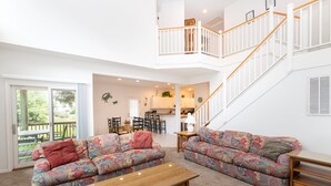 A spacious living area with a large sofa, a coffee table, and a staircase leading to an upper level. - Soundside- Golf Community, Priv Pool, Htub-MB3, How Sweet the Sound (Corolla)