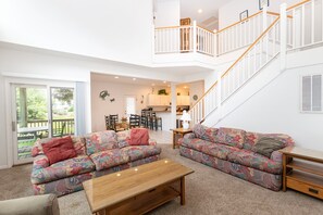 A spacious living area with a large sofa, a coffee table, and a staircase leading to an upper level. - Soundside- Golf Community, Priv Pool, Htub-MB3, How Sweet the Sound (Corolla)