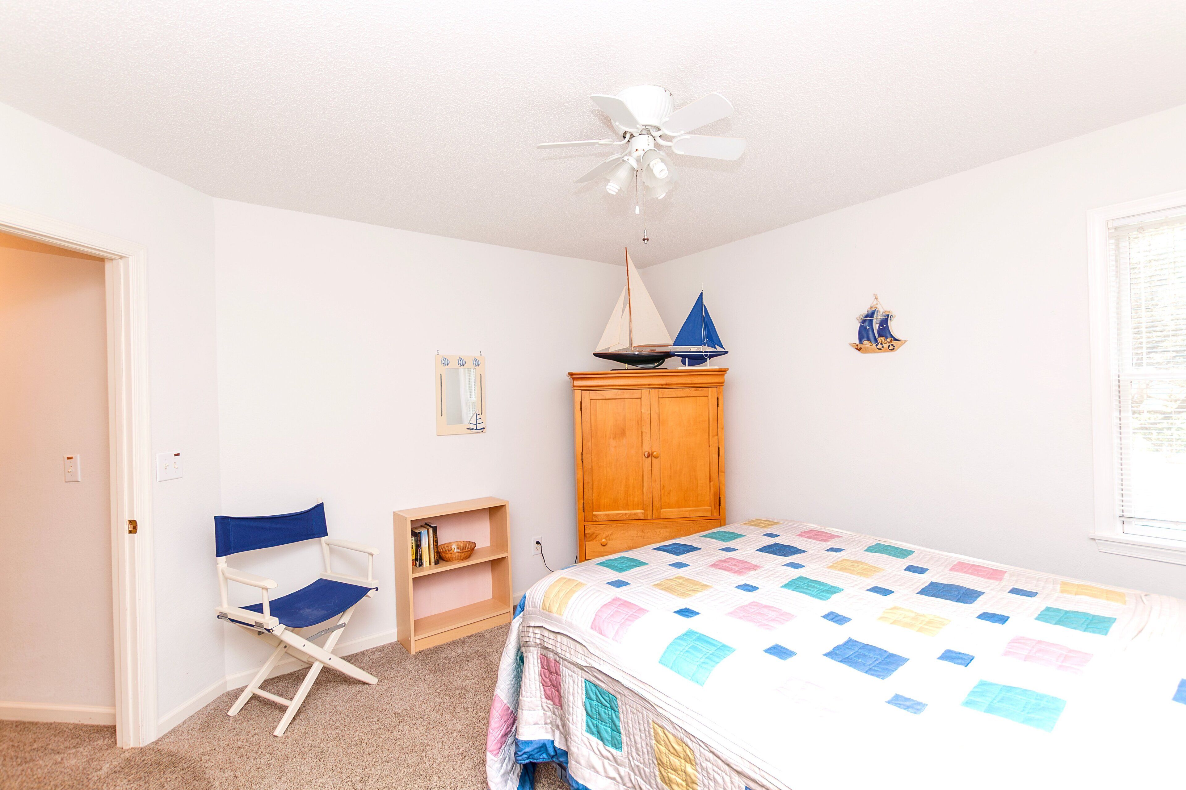 Une chambre à coucher comprenant un lit, une chaise, une armoire, un ventilateur de plafond et une petite décoration représentant un voilier.
