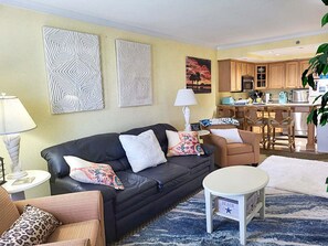 A living room with a black sofa, patterned cushions, a small white table, and a blue patterned rug. - Cozy Condo with Private Patio & Pool Access in Hatteras Village-  HIH212, Captain's Quarters (Hatteras)