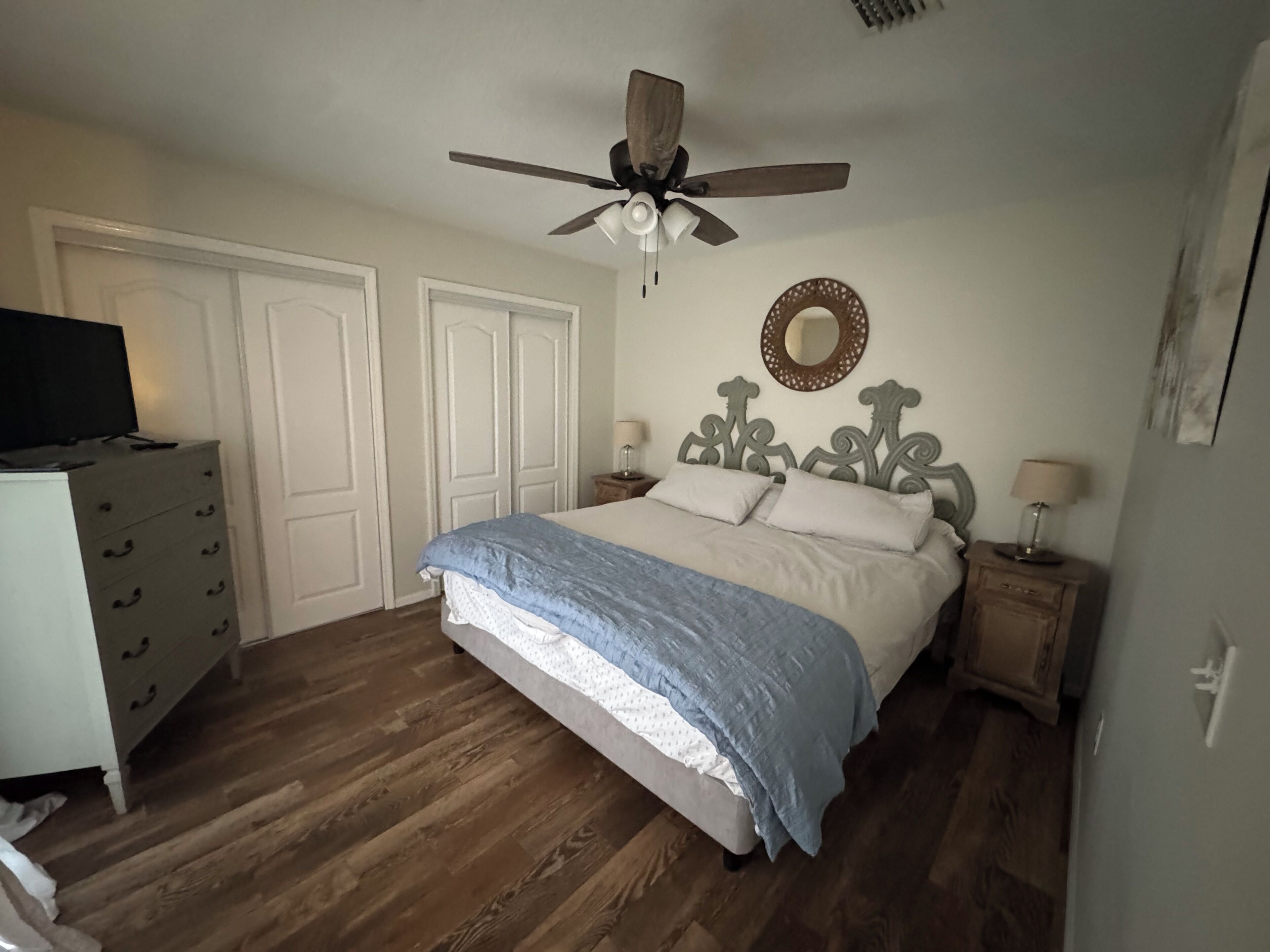 A bedroom with a bed, a ceiling fan, a dresser, and a nightstand with a lamp.