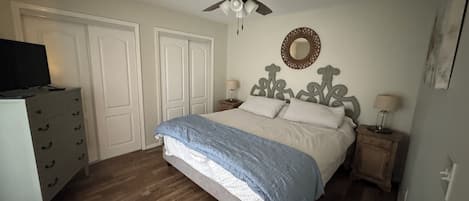 A bedroom with a bed, a ceiling fan, a dresser, and a nightstand with a lamp.