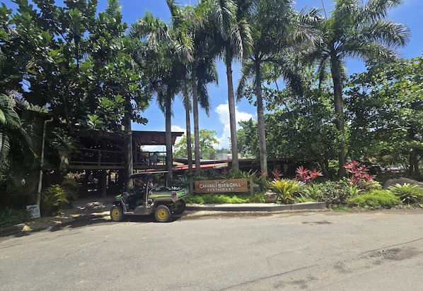 A restaurant with a signboard, surrounded by lush greenery and palm trees. - Oceanfront 1BR Condo with Stunning Beach Views & AC (Luquillo)