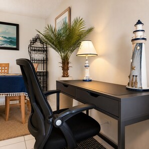 Un bureau avec une lampe, une plante en pot, un petit phare décoratif et une chaise.