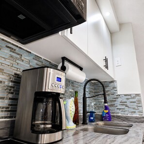A modern kitchen with a built-in coffee maker, a sink, and a backsplash with blue and white tiles. - Oceanfront 1BR Condo with Stunning Beach Views & AC (Luquillo)