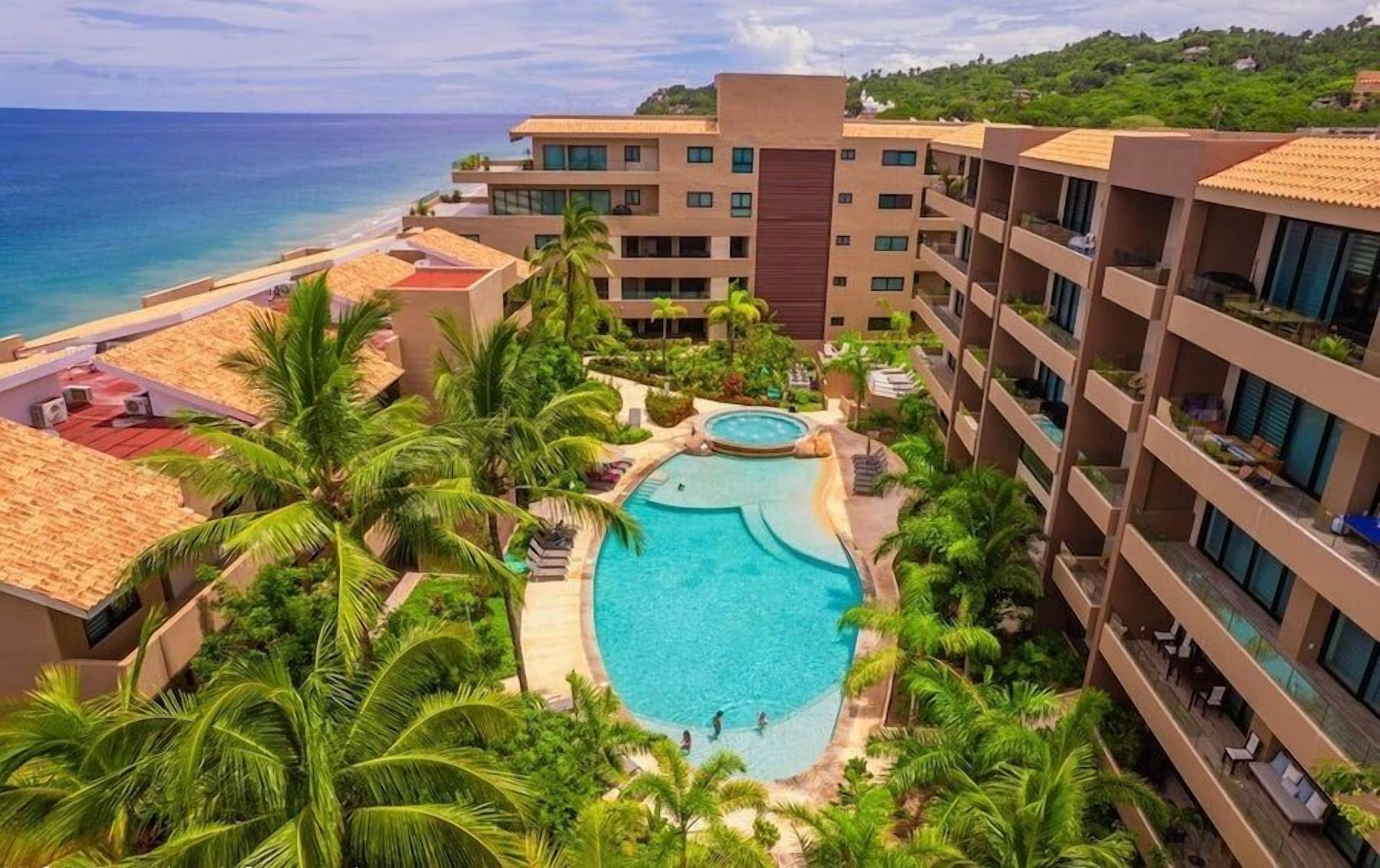 Un hotel con piscina central rodeada de palmeras y vistas al océano.