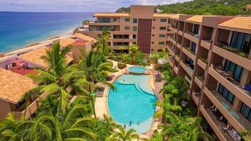 Un hotel con piscina central rodeada de palmeras y vistas al océano.