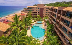 A hotel with a central swimming pool surrounded by palm trees and a view of the ocean. - Villa Orquídea (San Francisco)